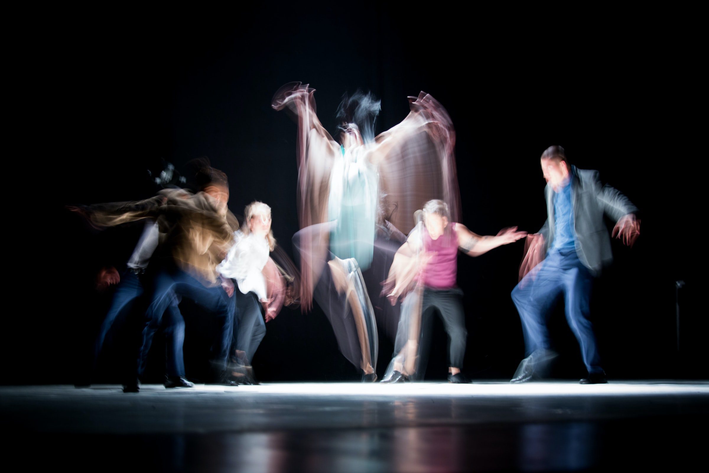 Community theatre ensemble — long-exposure photograph of dancers in motion on a black stage