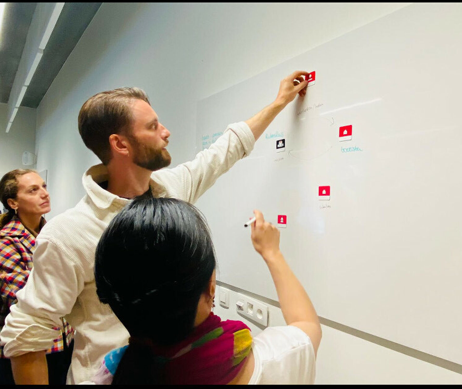 International cultural leaders collaborating in a workshop, placing red sticky notes on a whiteboard during an interactive training session focused on strategy and identity