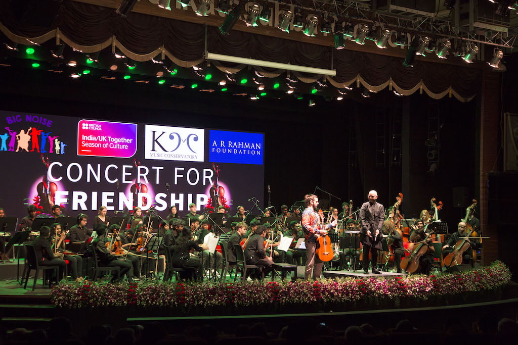 A Concert for Friendship featuring an orchestra performance with Indian and UK collaborators on stage, bright stage lighting and festive decor