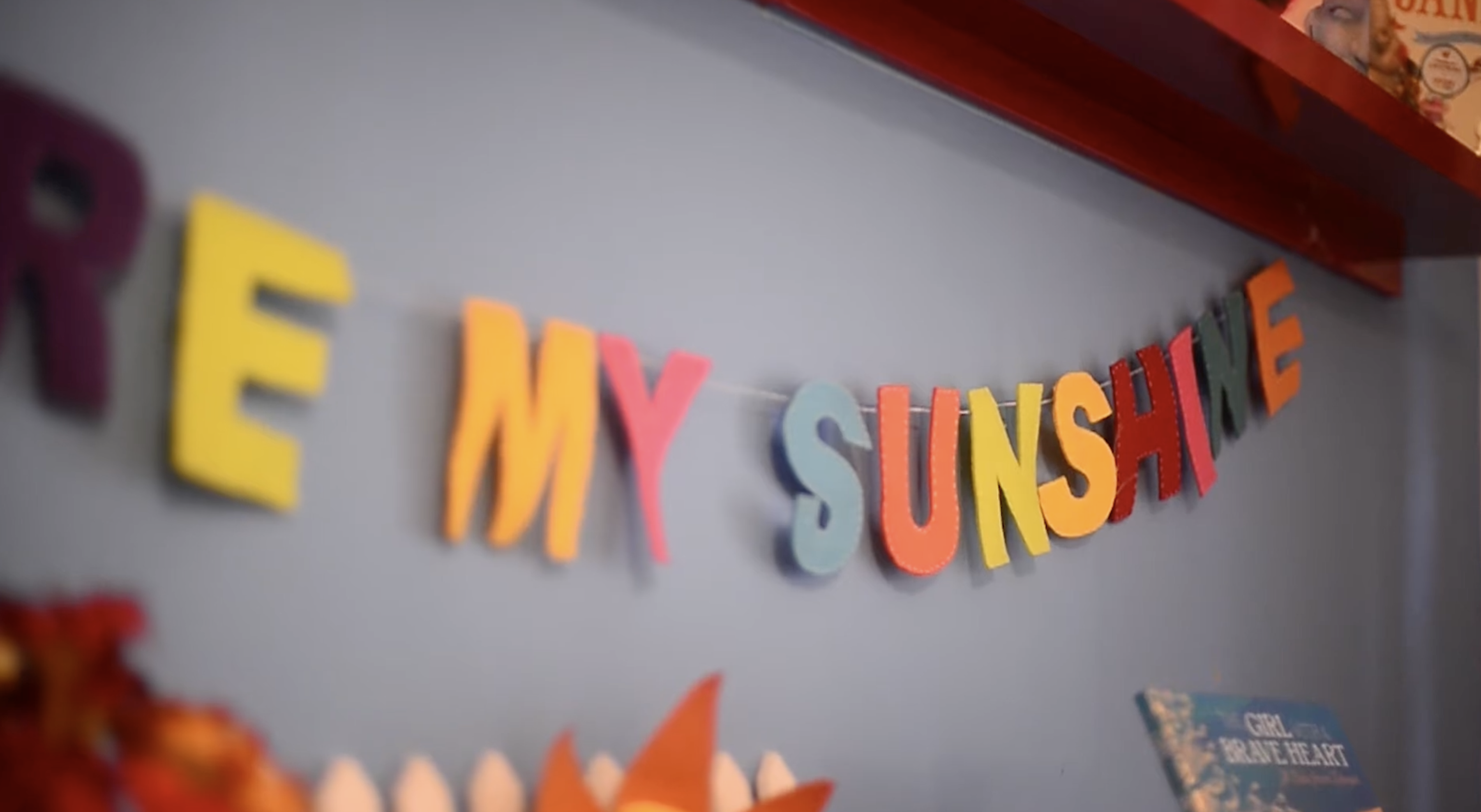 Colourful felt lettering spelling 'my sunshine' strung across a wall, with children's books on a shelf