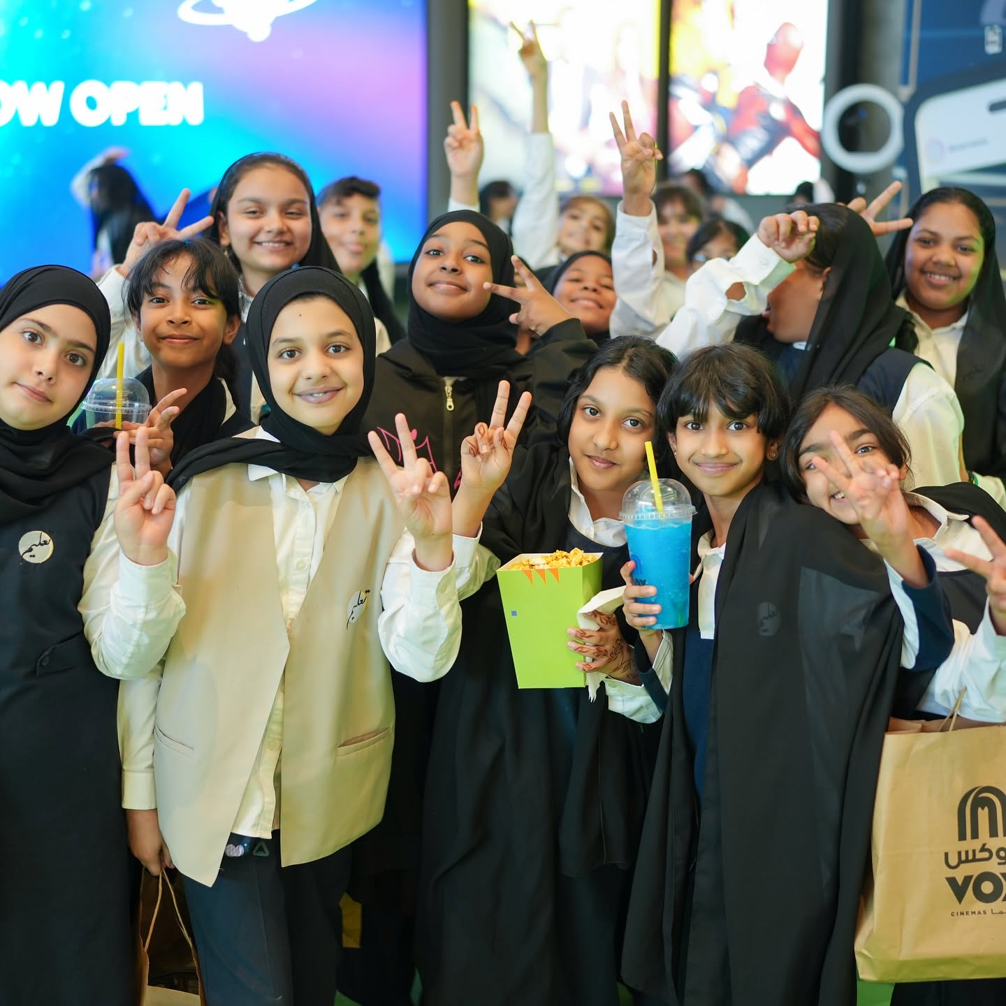 Schoolchildren flashing peace signs at a Sharjah International Children's Film Festival cinema screening, holding popcorn and drinks