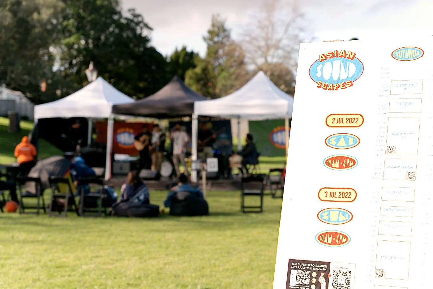 The ASIAN(SOUND)SCAPES programme board at Potters Park, Auckland, with the festival stage and marquees behind