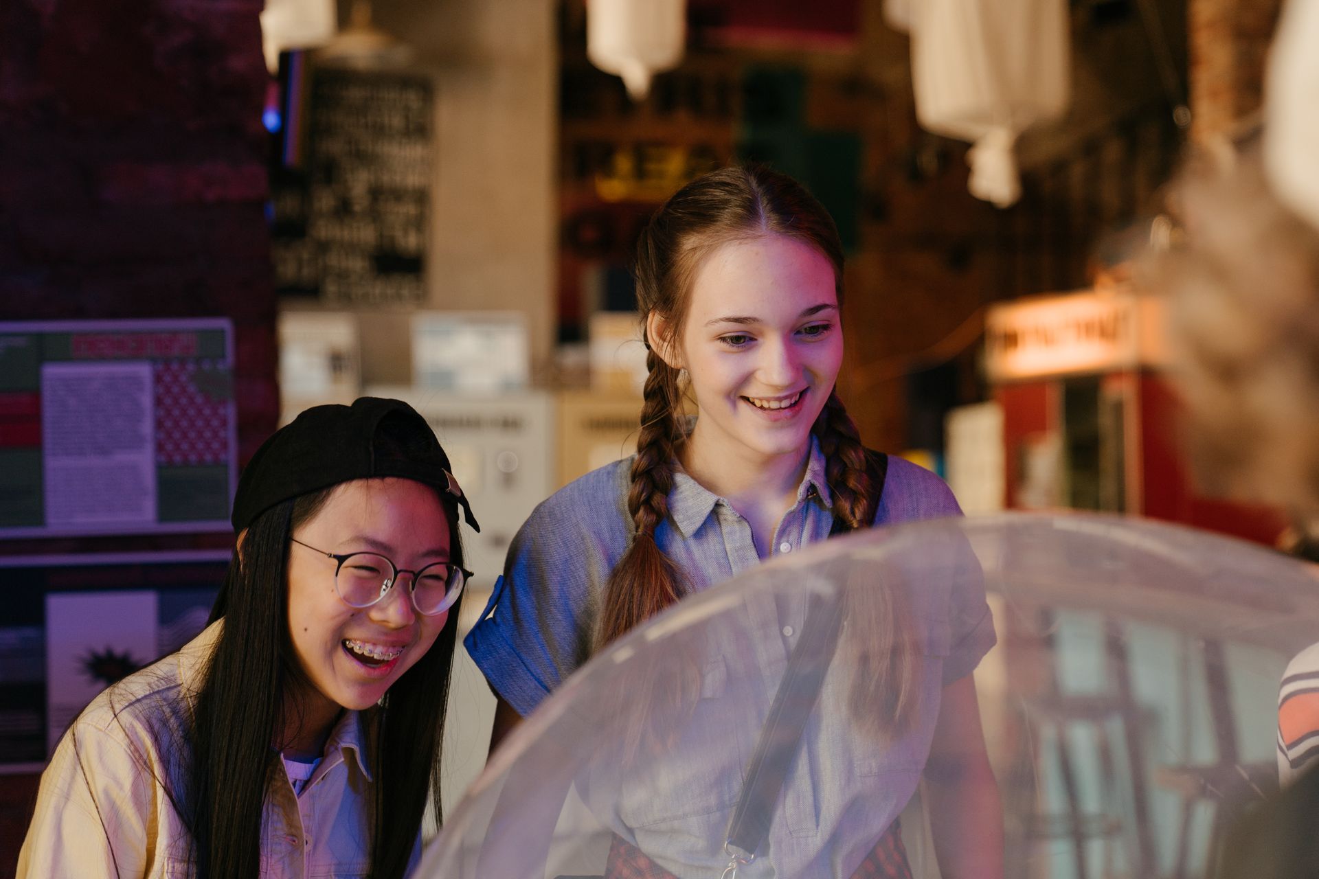 Two young people smiling and collaboratively viewing materials in a vibrant arts learning space with colorful lighting and creative materials